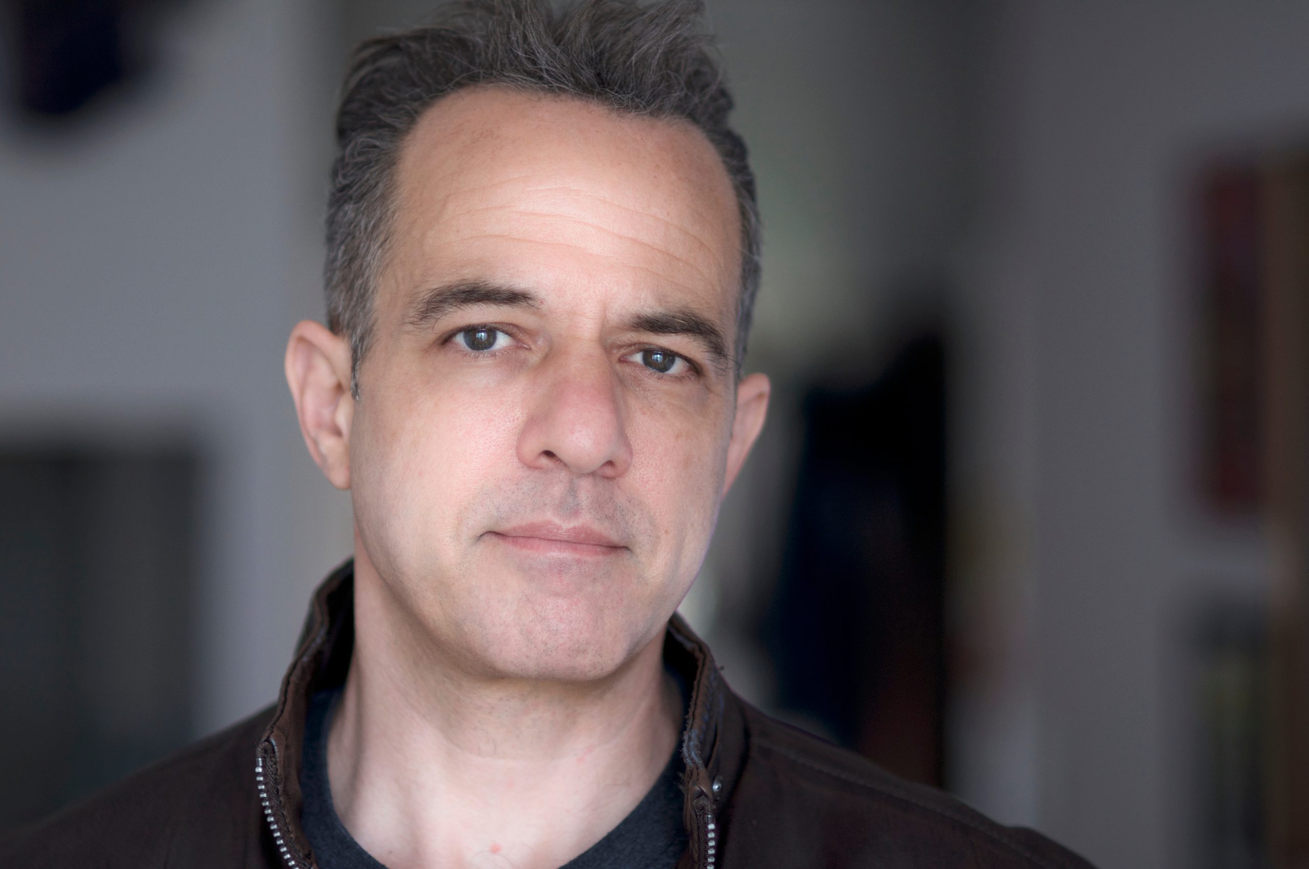 Headshot photo of David Mason in brown leather jacket with blurry background